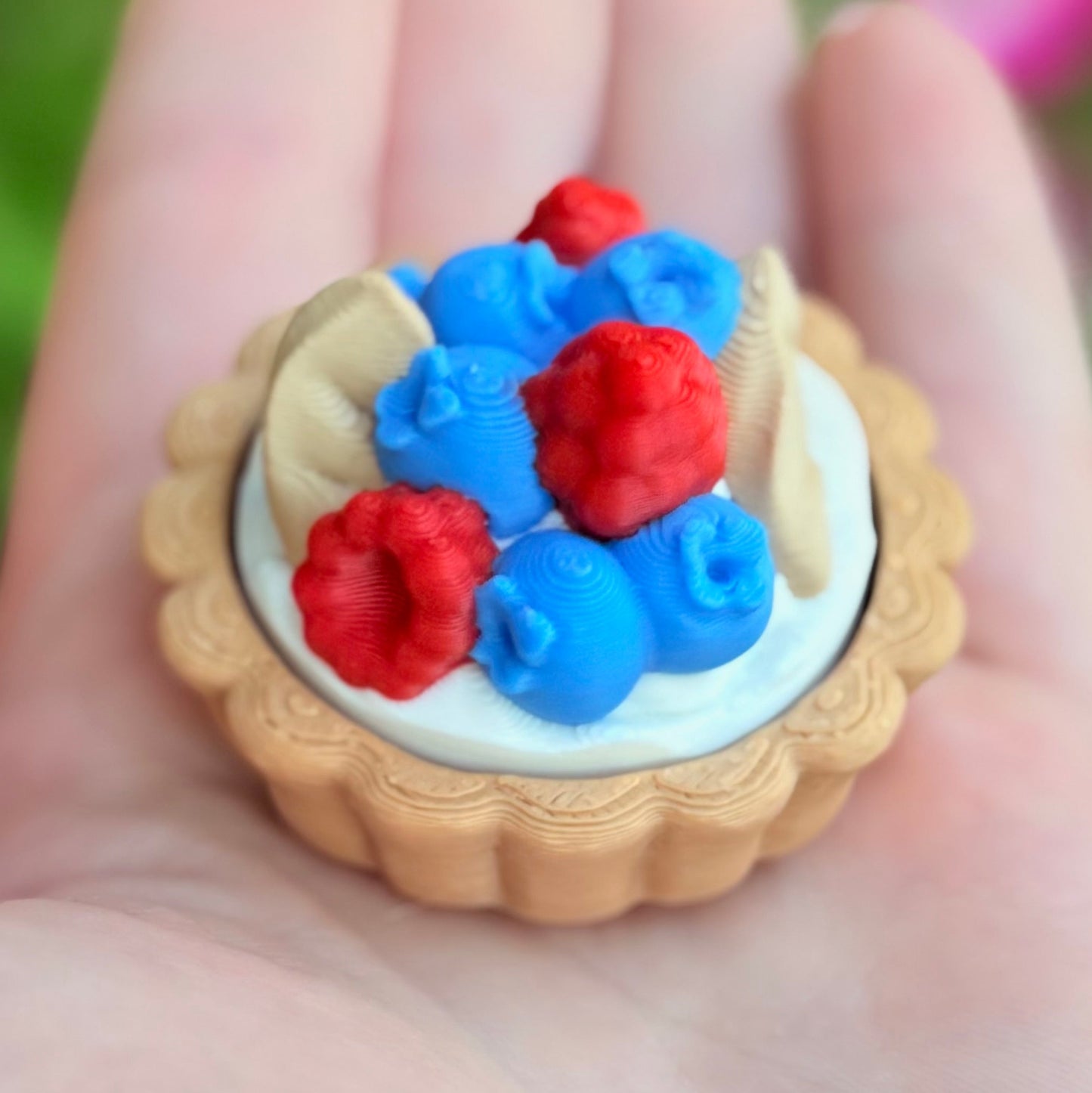 Miniature tart with red and blue berries held in a hand against a blurred natural background