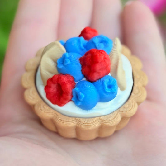 Miniature tart with red and blue berries held in a hand against a blurred natural background