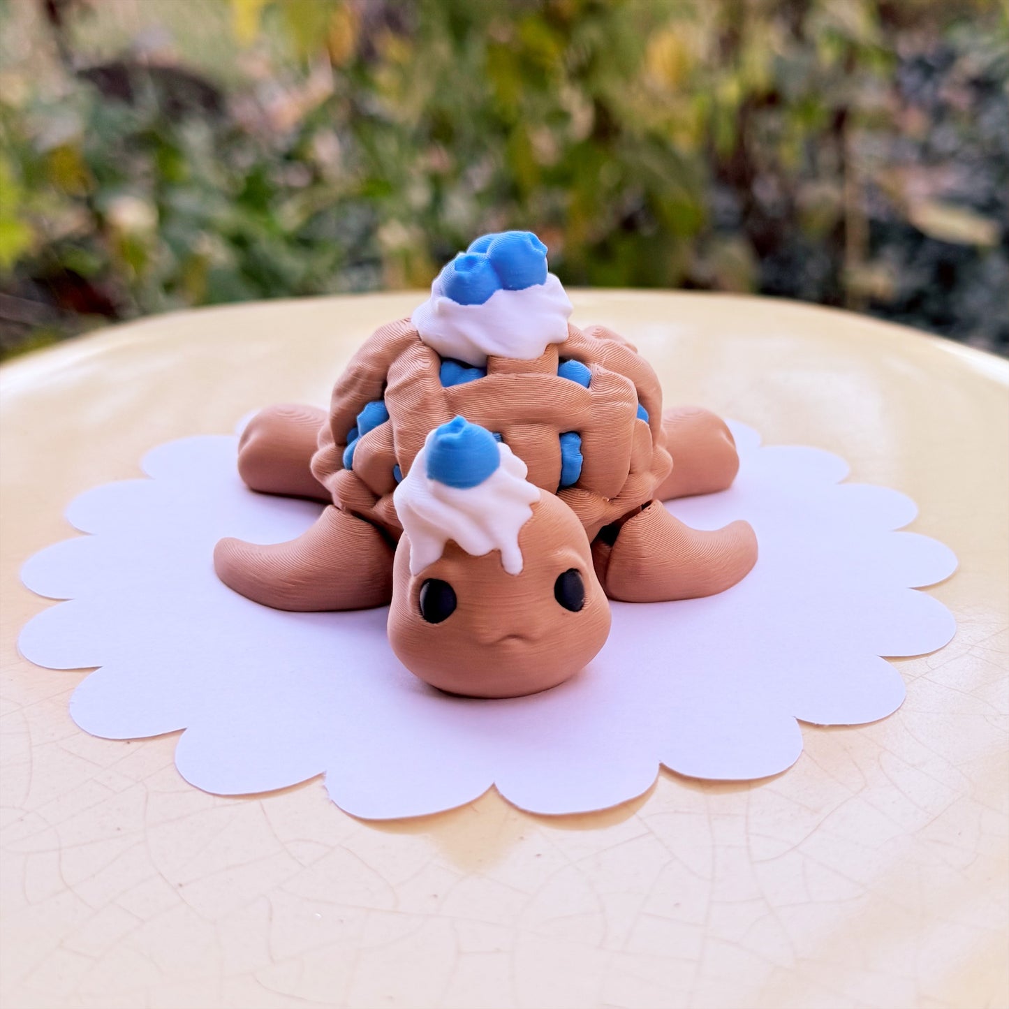 Toy turtle with whipped cream and blueberries on a white plate with a blurred green background